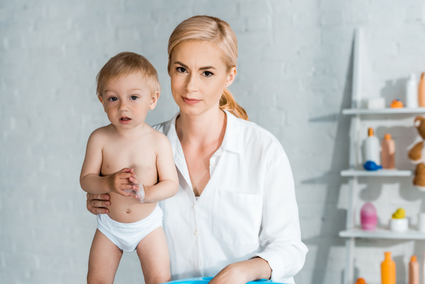 blonde woman looking at camera near cute toddler son at home  - Valokuva, kuva