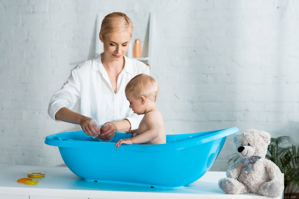 happy mother looking at cute toddler son taking bath at home  - Фото, изображение
