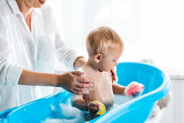 обрезанный вид на мать стирает милый ребенок сын в ванной комнате
  - Фото, изображение