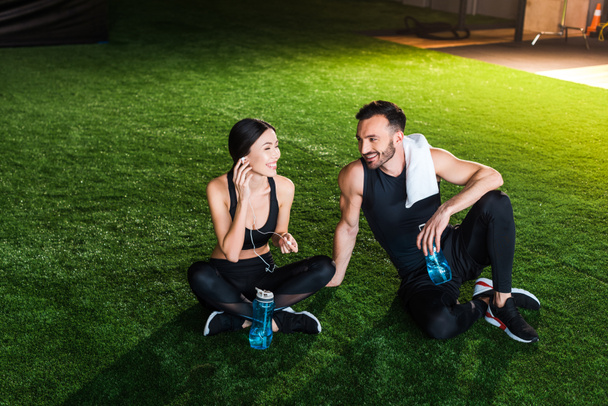 happy woman holding earphones and sitting on grass with handsome man  - Photo, Image