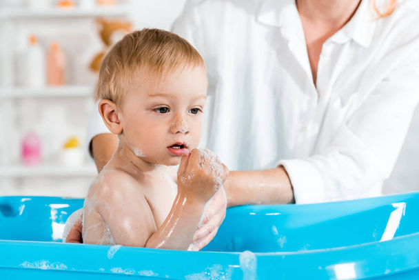 cropped view of mother washing cute toddler kid in baby bathtub  - Фото, зображення