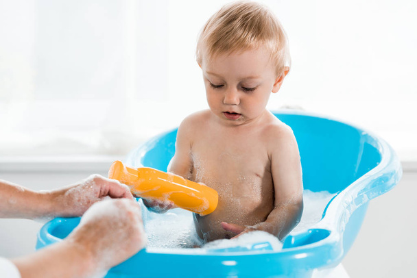 cropped view of mother near cute toddler son holding bottle with shampoo  - Foto, Bild