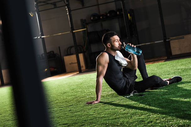 selective focus of man in sportswear drinking water while sitting on grass  - Photo, Image