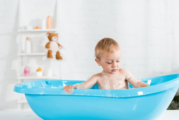 χαριτωμένο νήπιο παιδί που παίρνει μπάνιο και κοιτάζοντας τον αφρό μπάνιου  - Φωτογραφία, εικόνα