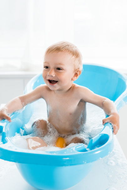 青い赤ちゃんのバスタブでお風呂に入っている間に笑顔幸せな幼児の子供  - 写真・画像