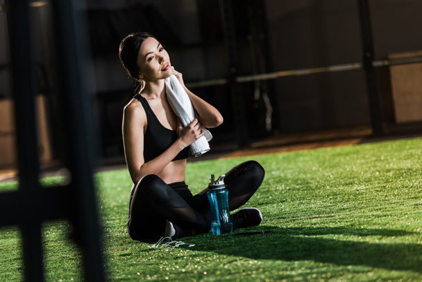 selective focus of athletic woman holding towel while sitting with crossed legs on grass  - Photo, Image