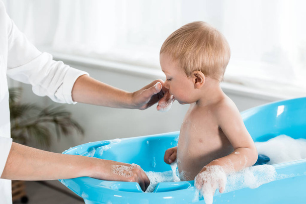 обрізаний вид матері торкається носа милого сина малюка у ванній кімнаті
  - Фото, зображення