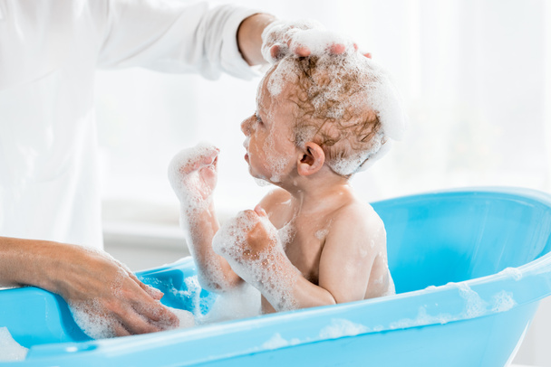 nyírt tekintettel az anya mosás fejét aranyos kisgyermek fia fürdőszobában  - Fotó, kép