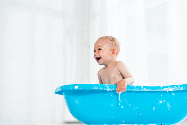 low angle view of cute toddler kid smiling in plastic baby bathtub  - Photo, Image