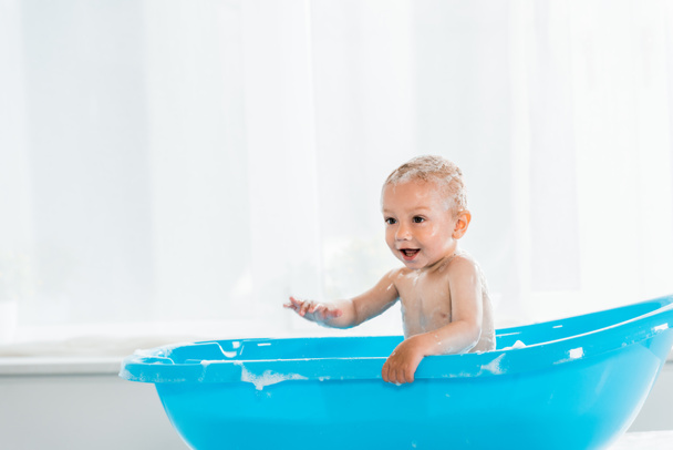 adorable toddler child taking bath and smiling in blue plastic baby bathtub  - Фото, изображение