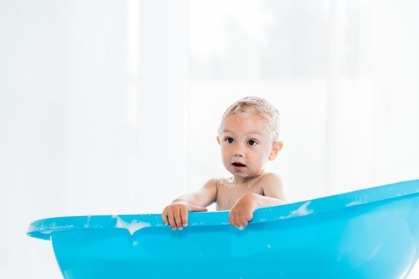 青いプラスチックの赤ちゃんのバスタブでお風呂を取る愛らしい幼児の子供  - 写真・画像