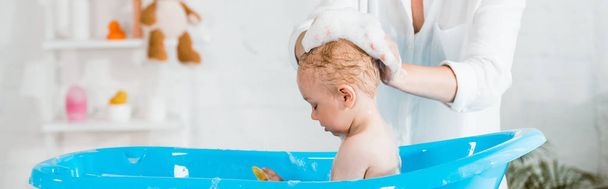 tiro panorámico de la madre cabeza de lavado de lindo hijo pequeño en el baño
  - Foto, Imagen