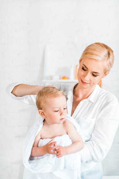 attractive blonde mother holding in arms toddler son in bathroom  - Фото, изображение