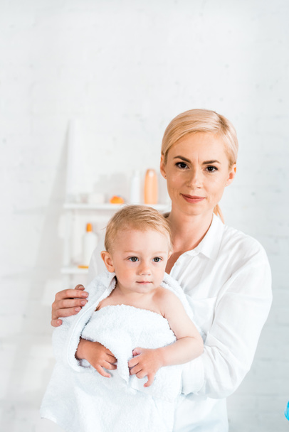 happy blonde mother holding in arms cute toddler son in bathroom  - Fotoğraf, Görsel