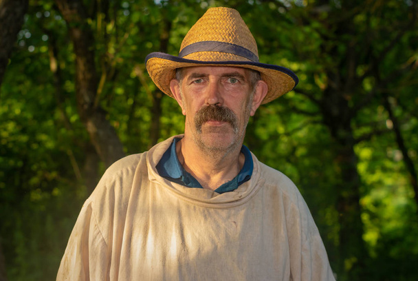 İş yerinde hasır şapka ve kirli keten gömlek giyen yorgun arı bakıcısı portresi - Fotoğraf, Görsel