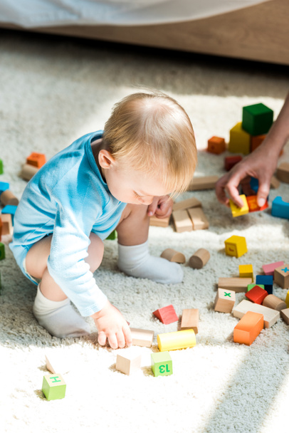 обрезанный вид женщины рядом с ребенком сын играет со строительством кирпича на ковре дома
  - Фото, изображение