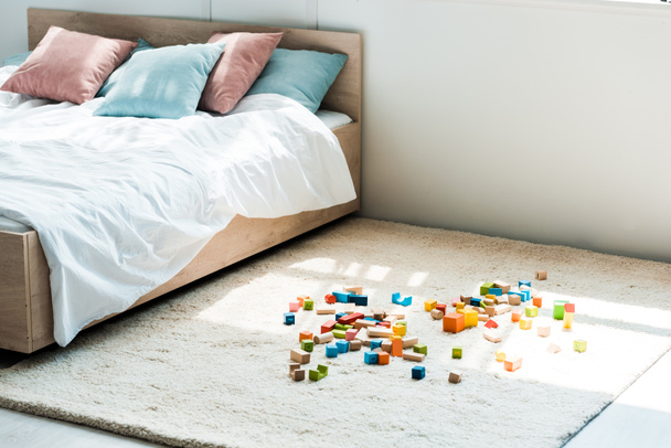 blocos de brinquedo perto da cama com cama branca, almofadas azuis e rosa
 - Foto, Imagem