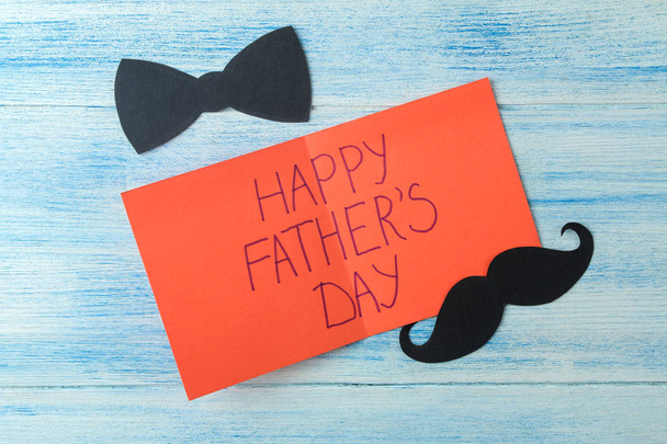 happy vader Day. Tekst en decoratieve mannelijke snor en strikje op licht blauwe houten achtergrond. Top View - Foto, afbeelding