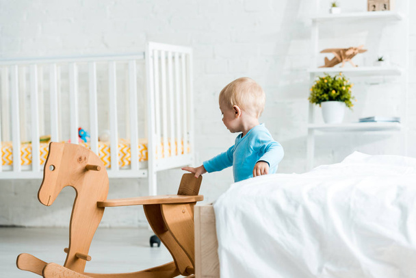 adorable toddler child standing near wooden rocking horse in modern bedroom  - Photo, Image