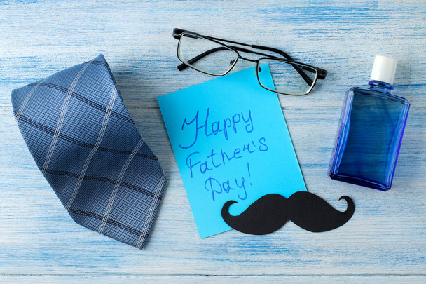 happy vader Day. tekst en mannen accessoires, stropdas, parfum en glazen op een licht blauwe houten achtergrond. Top View - Foto, afbeelding