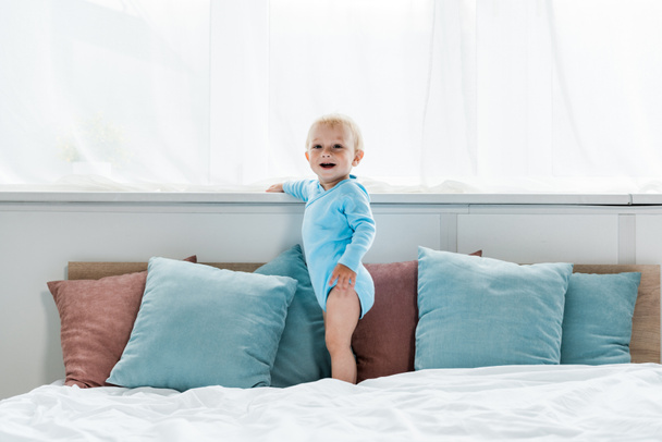 happy toddler kid standing on bed and smiling in bedroom  - Foto, imagen