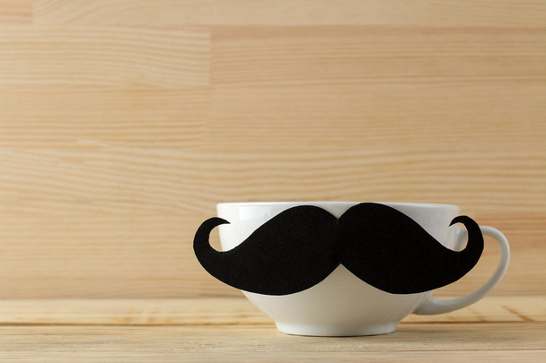Happy father's day. decorative male mustache on a white cup on a natural wooden background - Fotó, kép