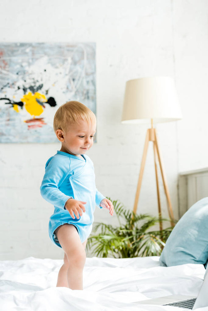 happy adorable toddler kid standing on bed near laptop  - Foto, Bild