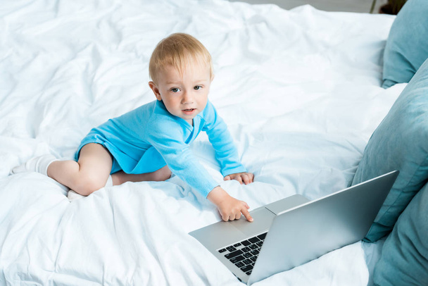 Widok z góry Cute dziecko Toddler wskazując palcem na laptopie, siedząc na łóżku w domu  - Zdjęcie, obraz