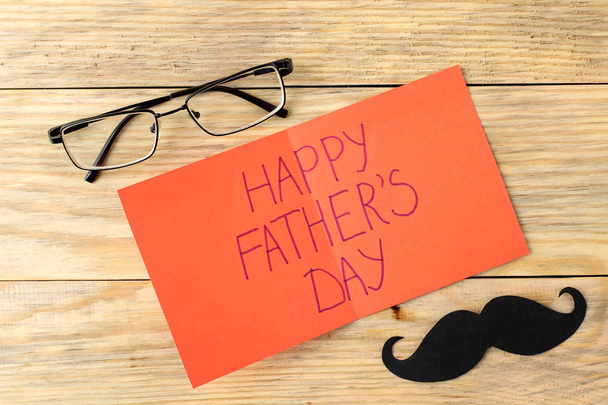 Happy father's day. text on paper and decorative mustache and glasses on a natural wooden background. top view - Fotó, kép