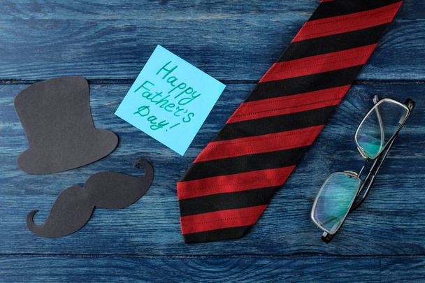 Joyeuse fête des pères. texte sur papier et cravate pour homme, verres et moustache décorative en papier et chapeau sur une table bleue en bois. vacances pour hommes. vue de dessus
 - Photo, image