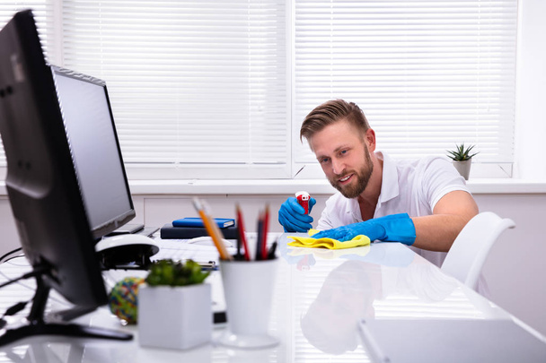 Janitor cleaning white desk in modern office - Фото, изображение