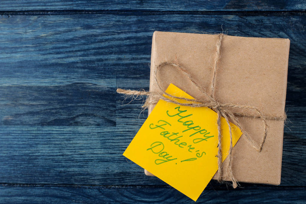 Счастливого дня отца. Текст на бумаге и подарок на голубом деревянном столе. мужской праздник. вид сверху
 - Фото, изображение