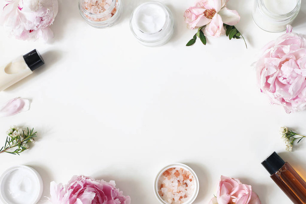 Styled beauty frame, web banner. Skin cream, shampoo, tonicum bottles, leaves, rose, peony flowers and salt on hite table background. Organic cosmetics, spa concept. Empty space, flat lay, top view. - Zdjęcie, obraz