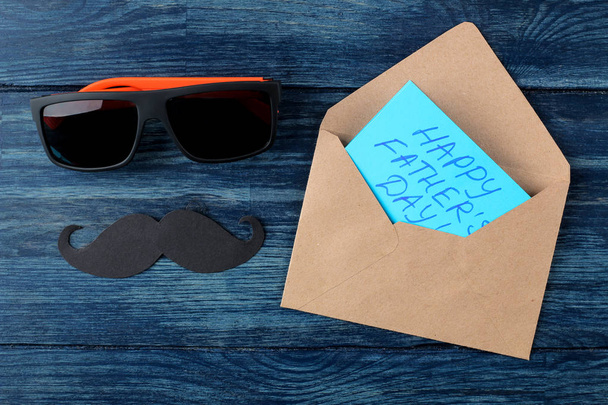 Glücklicher Vatertag. Text auf Papierbrille und Papierschnurrbart auf einem blauen Holztisch. Männerurlaub. Ansicht von oben - Foto, Bild