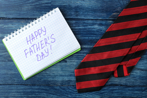 Szczęśliwy dzień ojca. Tekst w Notatniku i krawat na niebieskim drewnianym stole. wakacje dla mężczyzn. Widok z góry - Zdjęcie, obraz