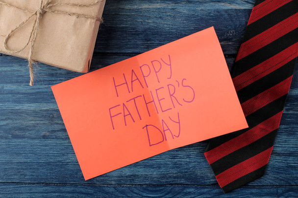 Szczęśliwy dzień ojca. Tekst na papierze, krawat i prezent na niebieskim drewnianym stole. wakacje dla mężczyzn. Widok z góry - Zdjęcie, obraz