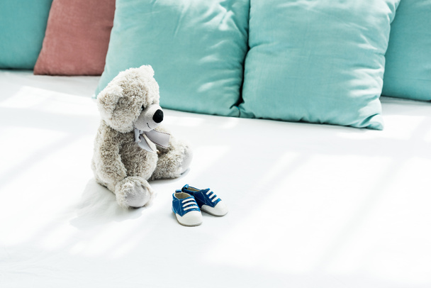 grey teddy bear near baby sneakers and pillows on white  - Photo, Image