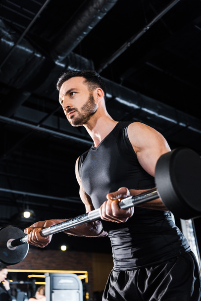 low angle view of athletic man working out with heavy barbell in gym  - Photo, Image