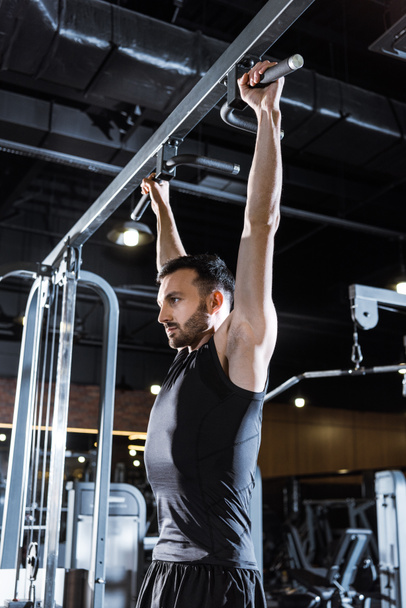 low angle view of handsome athletic man doing pull up in sports center  - Photo, Image
