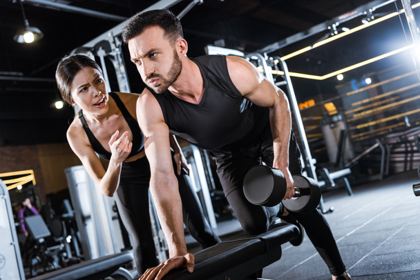 attractive trainer talking with bearded man working out with dumbbell  - Photo, Image