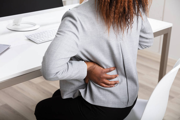 Side View Of African Businesswoman Holding Her Back While Working On Laptop At Office Desk - Photo, image
