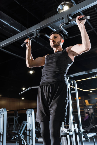 low angle view of athletic sportsman doing pull up in sports center  - Foto, imagen