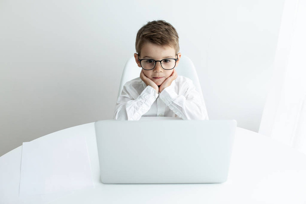 Mignon petit garçon en utilisant un ordinateur portable tout en faisant des devoirs sur fond blanc
 - Photo, image