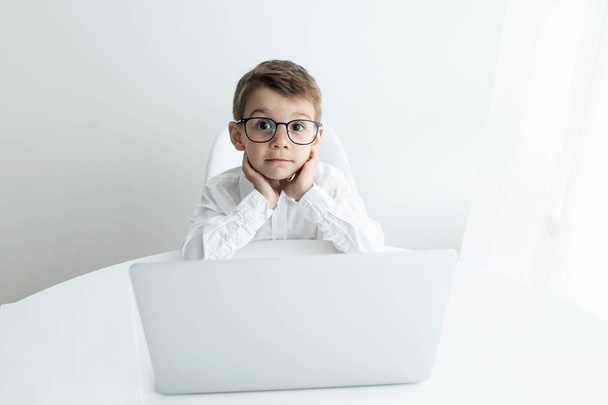 Cute little boy using laptop while doing homework against white background - Photo, Image
