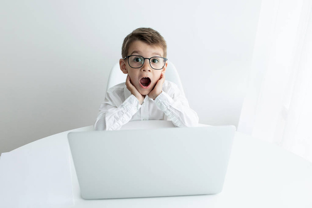 Aranyos kisfiú használ laptop, míg csinál házi ellen fehér háttér - Fotó, kép