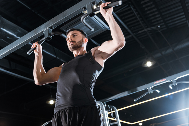 low angle view of handsome sportsman doing pull up in sports center  - Photo, Image