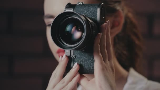 Pretty woman taking picture with vintage photo camera on brick wall background - Footage, Video