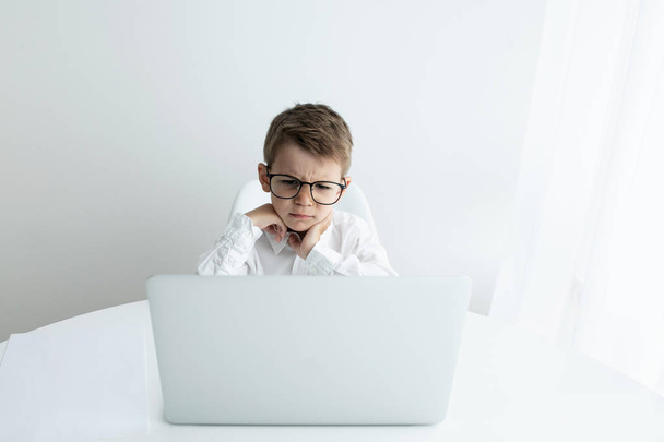 Cute little boy using laptop while doing homework against white background - Photo, Image