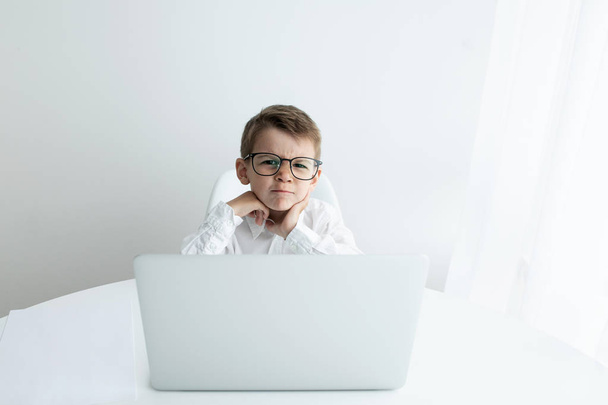 Cute little boy using laptop while doing homework against white background - Фото, зображення