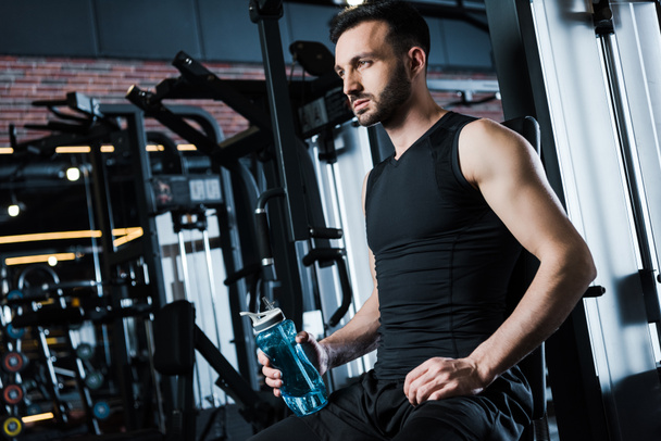 low angle view of handsome sportsman in sportswear holding sport bottle in gym  - Photo, Image